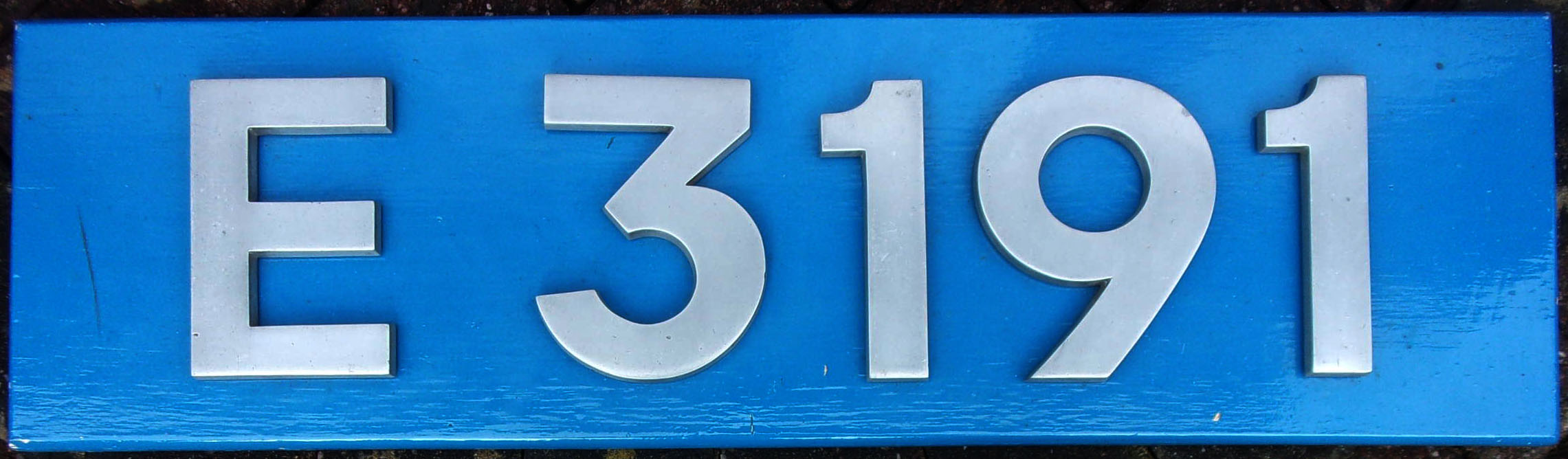 AC Electric Locomotive Cabside Number "E3191", as carried by Class 86, built English Electric, Vulcan Foundry, emerging to traffic in 1965, later renumbered Tops "86201" in 1972, then "86101" in 1974, named Sir William A. Stanier F.R.S. in 1978. Numbers mounted on wooden board. 32" x 9".